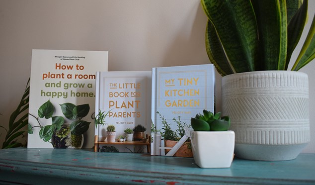 Three books about plants on a teal shelf next to plants.