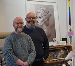 Two men standing in front of a picture of the model Kate Moss in a crown behind a shop counter