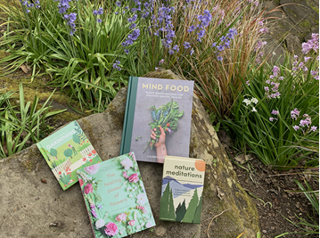 Four books on a rock surrounded by wildflowers