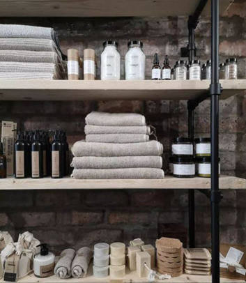 Products including towels and lotions neatly assembled on black shelving against an exposed brick wall.