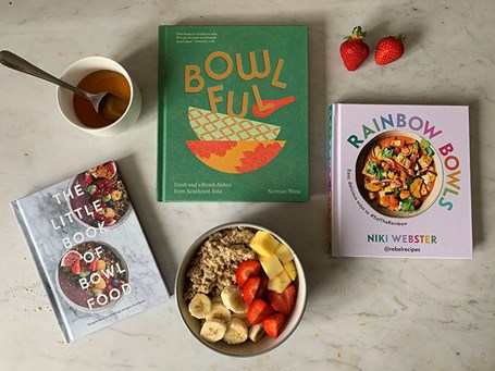 Books about bowl food laid out on a faux-marble surface surrounded by food items.