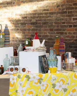 Curated seletion of crockery on a yellow 1970s tablecloth in a retail setting.