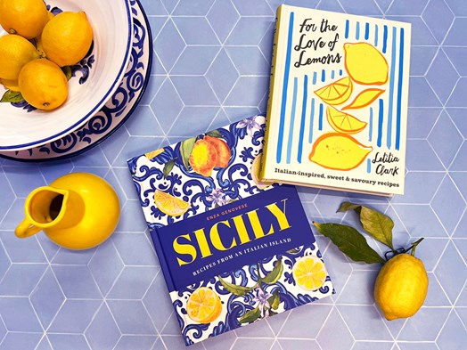 Italian cookbooks on a blue backdrop surrounded by lemons