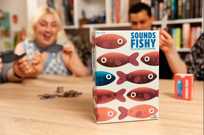 Sounds Fishy board game in foreground with adults playing in the background.