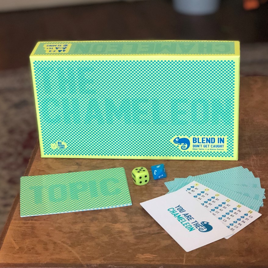 Green Chameleon board game sitting on a brown table surrounded by the contents of the game including cards and dice